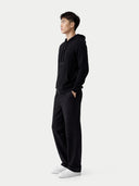 Person standing sideways wearing a black hoodie and pants on a white background #color_black