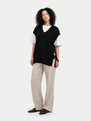 Woman wearing a black sleeveless maternity sweater over a white shirt with beige pants on a white background #color_black
