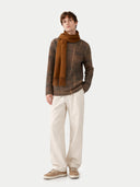 Man wearing a brown plaid sweater, beige scarf, white pants, and brown shoes on a white background #color_otter