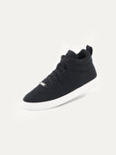 A high-top sneaker featuring a black textured upper with matching black laces and a small silver brand plate at the base of the tongue. The shoe has a padded collar, a pull tab at the heel, and a thick white rubber sole, shown from a three-quarter angle against a plain white background. #color_black