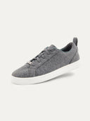 A three-quarter view of a low-top sneaker featuring a heather gray felted or textured knit upper with matching gray laces. The shoe includes a small silver brand plate at the base of the tongue, a gray pull tab at the heel, and a thick, solid white rubber sole, set against a plain light background. #color_stone-gray