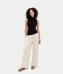 Front view of a woman standing with a black sleeveless mock neck cashmere top and white wide-leg pants. shop women