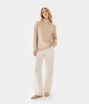 Front view of a woman standing with a beige turtleneck cashmere sweater and white wide-leg pants. shop women