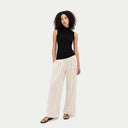 Front view of a woman standing with a black sleeveless mock neck cashmere top and white wide-leg pants. shop women