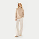 Front view of a woman standing with a beige turtleneck cashmere sweater and white wide-leg pants. shop women