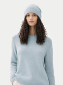Woman wearing a light blue sweater and matching beanie against a white background #color_cloud-blue
