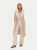 Woman wearing a long beige vest over a cream outfit on a white background #color_warm-grey