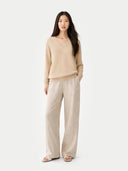 Woman wearing a beige sweater and pants on a white background.