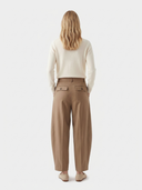 back view of a woman wearing beige pants and a white sweater on a light gray background. #color_dark-brown