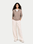 Woman wearing a brown zip-up hoodie and white pants on a white background #color_taupe