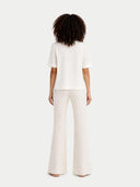 back view of a person wearing a white outfit with wide-leg pants on a light gray background #color_whisper-white