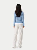 Woman wearing a light blue sweater and white pants on a plain background #color_dusty-blue