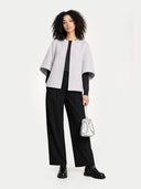 Woman wearing a light gray poncho over a black outfit, holding a silver handbag on a white background #color_arctic-ice