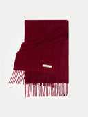 A deep burgundy wool scarf with fringe detailing and a small gold-tone metal brand tag reading 'GORI', displayed on a clean white background. bordeaux