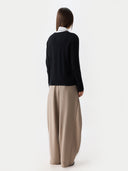 back view of a woman wearing a black cardigan and beige pants on a white background #color_black