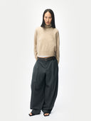 Person wearing a beige sweater and dark gray wide-leg pants on a white background #color_warm-grey