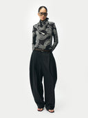 Person wearing a black and white patterned top with high-waisted black pants on a white background. #color_black