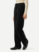 Side view of a person wearing black pants and a beige sweater on a white background #color_black