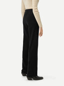 Back view of a person wearing black pants and a beige top on a white background #color_black