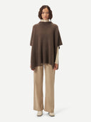 front view of a woman wearing a brown poncho over a white turtle neck sweater and beige leather pants #color_cocoa