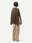 back view of a woman wearing a brown poncho over a white turtle neck sweater and beige leather pants #color_cocoa