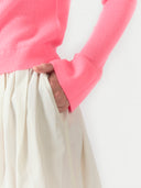 Person wearing a pink sweater and white pants against a light background #color_shell-pink