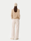 back view of a woman wearing a beige sweater, white pants and a beige beanie on a white background #color_beige