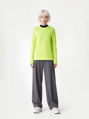 Person wearing a bright green sweater and gray pants on a white background #color_sunny-lime