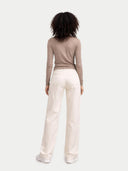 back view of a person wearing a beige long-sleeve top and white pants on a light gray background #color_timber-wolf