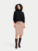 front view of woman wearing a black sweater, beige skirt, and brown boots on a white background #color_black