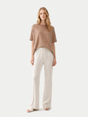 Woman wearing a brown top and white pants on a white background #color_timber-wolf
