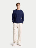 Man wearing a navy sweater and white pants on a light gray background #color_navy-blazer