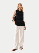 Woman wearing a black sleeveless top with ruffled details and white pants on a light gray background #color_black