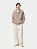 Person wearing a beige hoodie and white pants on a plain background #color_taupe