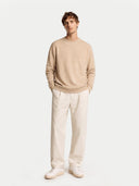 front view of a man wearing a beige sweater and white pants on a light gray background #color_warm-grey