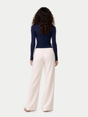back view of a woman wearing a navy long-sleeve top and white pants on a light gray background. #color_dark-indigo #ai-image