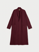 A long-sleeved, open-front coat in deep burgundy, featuring a shawl collar and large front patch pockets, displayed flat against a light gray background.