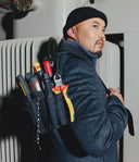 Man wearing a tool belt with various tools against a white wall.