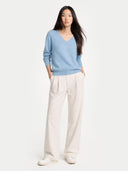 front view of a Woman wearing a light blue v-neck sweater and white pants on a white background #color_light-blue