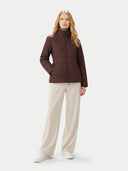 Woman wearing a brown quilted jacket and beige pants on a white background #color_vineyard-wine