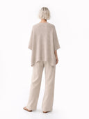 back view of a person wearing a beige poncho and pants on a white background #color_biscotti
