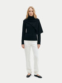Woman wearing a black with scarf-neck sweater and white pants on a white background #color_black