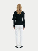 back view of a woman wearing a black sweater and white pants on a white background #color_black