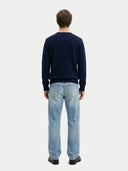 back view of a man wearing a navy sweater and light blue jeans on a white background #color_navy