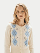 Woman wearing a cream cardigan with blue argyle pattern on a light background #color_coconut-milk