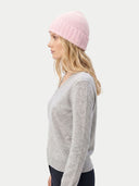 side view of a woman wearing a pink beanie and gray sweater on a white background. #color_pink