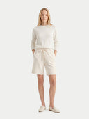 Woman wearing a white sweater and cream shorts on a white background. #color_pure-white
