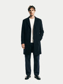 Man wearing a dark coat over a white shirt on a plain background. #color_black