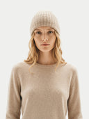 close up of a woman wearing a beige knit crew neck sweater and beanie against a white background #color_beige