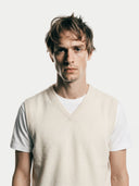 close up of a man wearing a beige v-neck sweater vest over a white shirt on a plain background #color-white